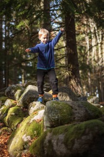 7 year old boy walks on rocks in the mountain forest
