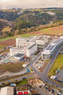Modern industrial buildings in hilly suburban landscape, surrounded by forest and fields, shortly