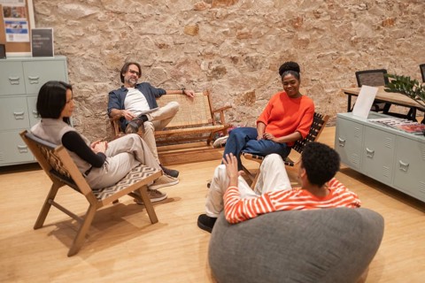 A group of diverse professionals engaging in a casual conversation in a modern coworking space with