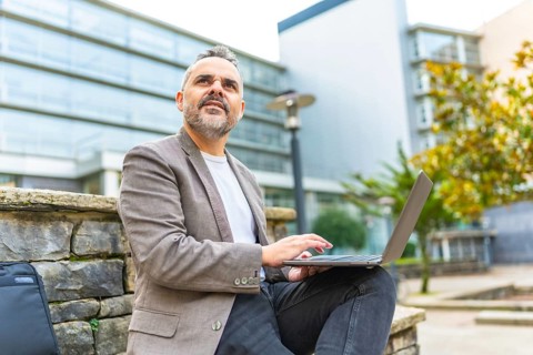 Confident mature caucasian businessman using laptop sitting on urban bench