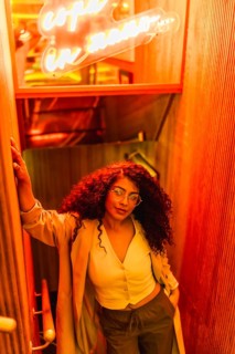 Vertical high angle view portrait of a latin woman in glasses against red neon sign looking at