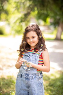 A joyful little girl smiling with chamomile flowers in her hair, enjoying the sunny outdoors. Her