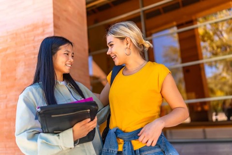 Happy female multi-ethnic university students talking outside the university building