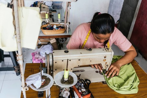 A asian seamstress focuses intently on sewing fabric using a vintage machine. The workshop is