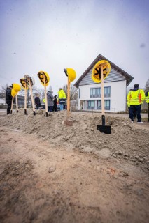 Spade with helmets in a pile of sand, several people and a building in the background, fiberglass
