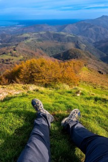 Hiker resting on grassy mountaintop, enjoying breathtaking views of rolling hills, colorful