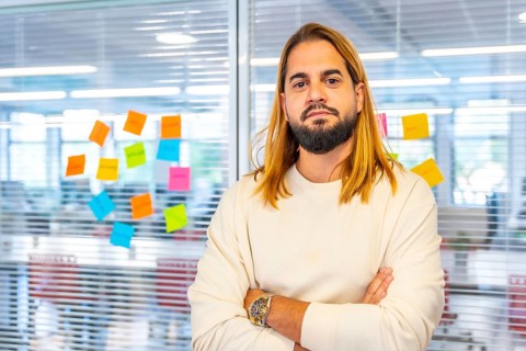 Portrait of a creative and young man standing with arms crossed next to a glass with adhesive notes