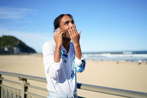 A man, exuding pride and happiness, is captured on the phone at a sunny beach. His expression and