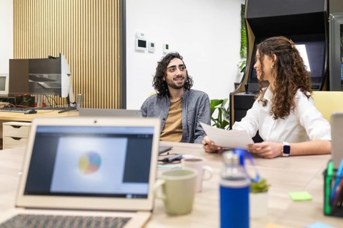Professionals engaging in a collaborative discussion in a modern open-plan office. Laptops and