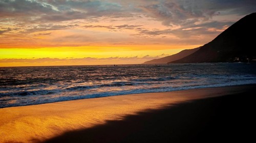 Golden yellow sunset, beach with volcanic sand on a calm sea with mountains in the background,