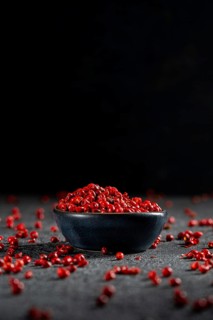 A dark bowl filled with vibrant red peppercorns is set against a textured, dark grey background.