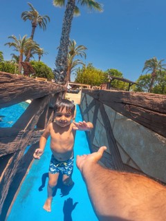 Happy child enjoying a waterslide and reaching for parent's hand at a water park, summer vacation