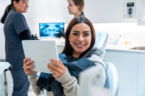 Smiling woman holding a mirror in a dentist chair, expressing satisfaction with dental results