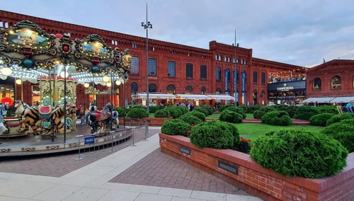 Amusement carousel and red brick façade with manicured bushes at dusk, Manufaktura, Lódz, Lodz,