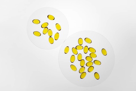 Bright yellow omega-3 and vitamin D capsules displayed on two white surfaces, highlighting their