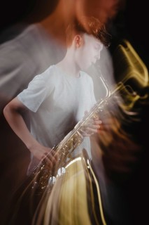 A teenage boy passionately plays a saxophone in a dimly lit studio, with dramatic lighting creating