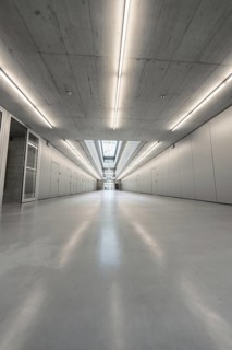 An elongated, well-lit corridor with concrete walls showing central elements of modern, minimalist