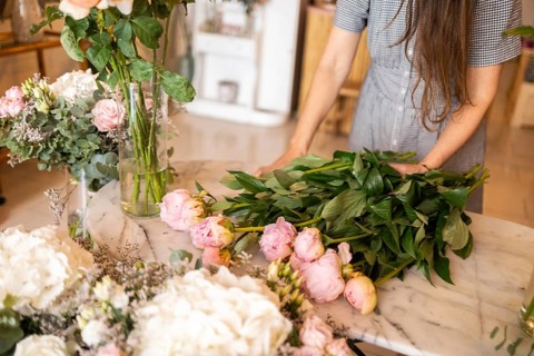 A woman arranges fresh pink and white flowers on a marble table in a cozy flower shop. The vibrant