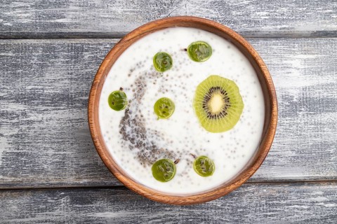 Yogurt with kiwi, gooseberry, chia and almonds in wooden bowl on gray wooden background. top view,