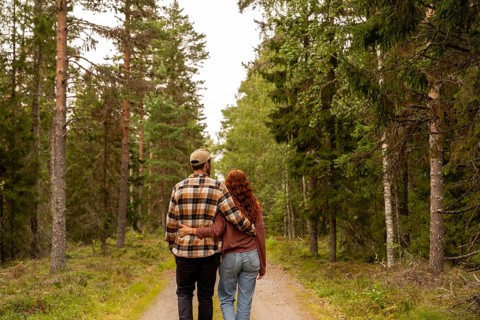 A couple embraces while walking through a lush green forest path in Sweden, surrounded by tall