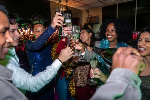 Group of diverse friends standing together, smiling and toasting with champagne glasses while