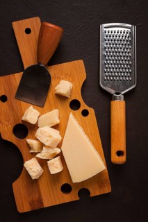 Hard cheese, parmesan, on a cutting board, cheese knife, grater, top view, no people