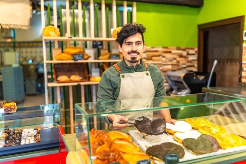 Latin man serving chocolate puff pastry palm in a bakery shop