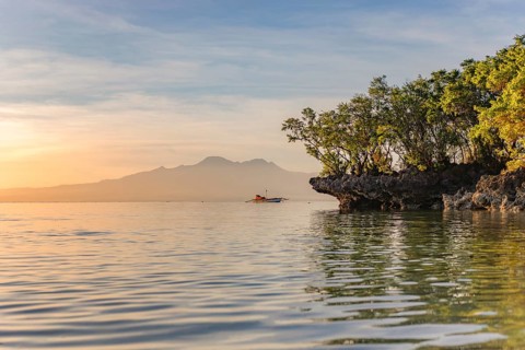 Sunrise illuminates a serene seascape in the Philippines with a boat nearby and mountains in the