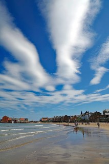 Sandy beach beach with impressive clouds and blue sky, surrounded by coastal buildings and people,