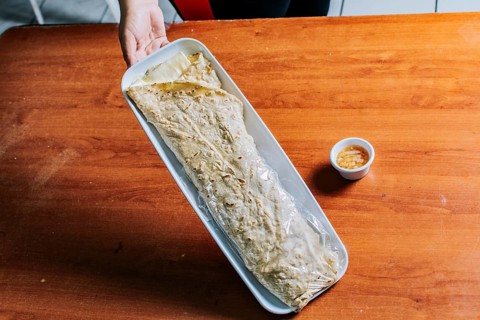 Hand holding a traditional quesillo served on wooden table. Top view of Nicaraguan Quesillo on a