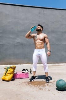 Fit man taking a break during outdoor workout, hydrating with a bottle of water under the sun. Gym
