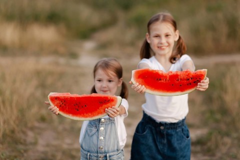 Two smiling children holding large slices of juicy watermelon outdoors. The bright, sunny day
