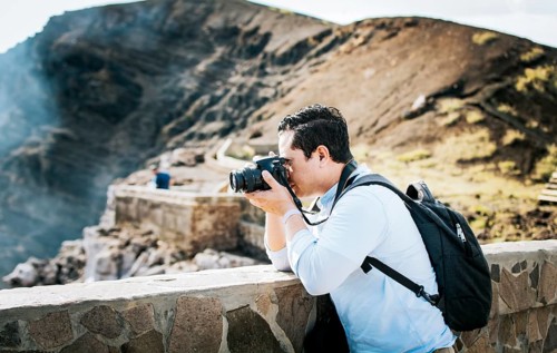 Close up of tourist man taking photos at a volcanic viewpoint. A tourist man with a photo camera