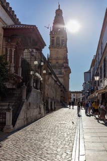 Street with church tower in the background, people walking in sunlight with long shadows, Cordoba