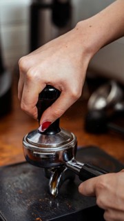 A barista's hand masterfully tamping espresso beans with a tamper, demonstrating the art of