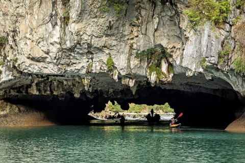 Kayakers explore an impressive rock formation with an arch over glittering water, natural scenery