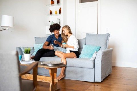 A joyful couple relaxing on a cozy sofa at home, chatting and sharing a moment of happiness. The