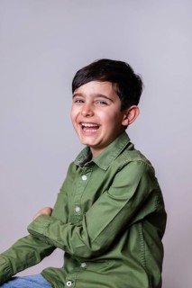 A joyful young boy with dark hair and a big smile, dressed in a green shirt and light blue jeans,