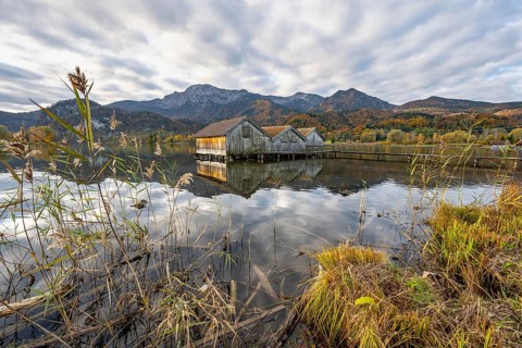Boathouses in the lake at sunrise, Lake Kochel in autumn with reflection, mountain peaks