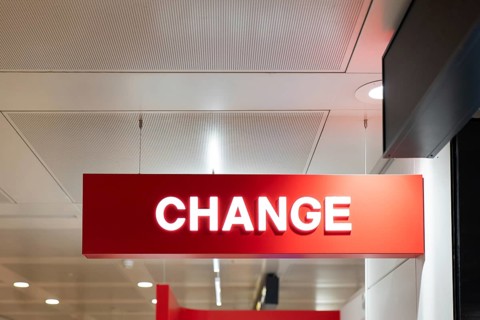 A red sign displaying the word CHANGE hangs from the ceiling of an airport terminal. The bright