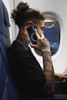 A young woman with detailed tattoos on their arms and neck uses a smartphone while seated on an
