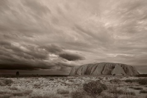 Dark threatening rain clouds hang over Uluru (Ayers Rock), black and white, sepia, monochrome,