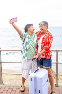 Two joyful mature lesbians taking a selfie together by the seaside, ready to start their summer