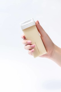 A close up image of a hand holding a roll on waxing cartridge, ideal for hair removal. The