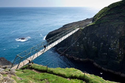 Hiker standing on the so-called Atlantic Bridge, footbridge over a crevice Hólmgjógv, Mykines,