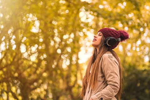 Portrait of a woman in autumn in a forest with brown leaves with her eyes closed listening to music