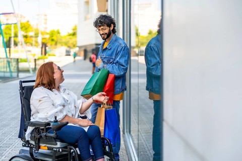 Young man holding shopping bags and talking to a smiling woman sitting in a wheelchair on a city