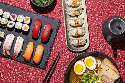 Overhead shot of a Japanese food table with sushi, ramen, dumplings, and tea, captured with strong