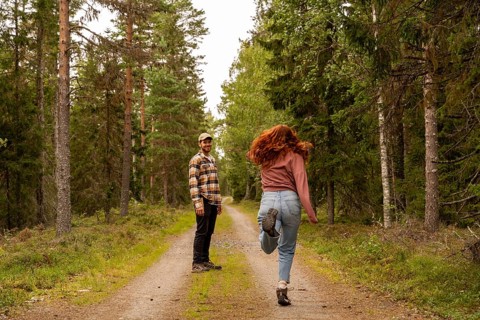 A couple enjoys a leisurely walk along a dirt path in a Swedish forest. The man smiles while the