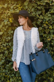 A stylish woman models a casual outfit featuring a fluffy white vest, patterned blouse, jeans, and